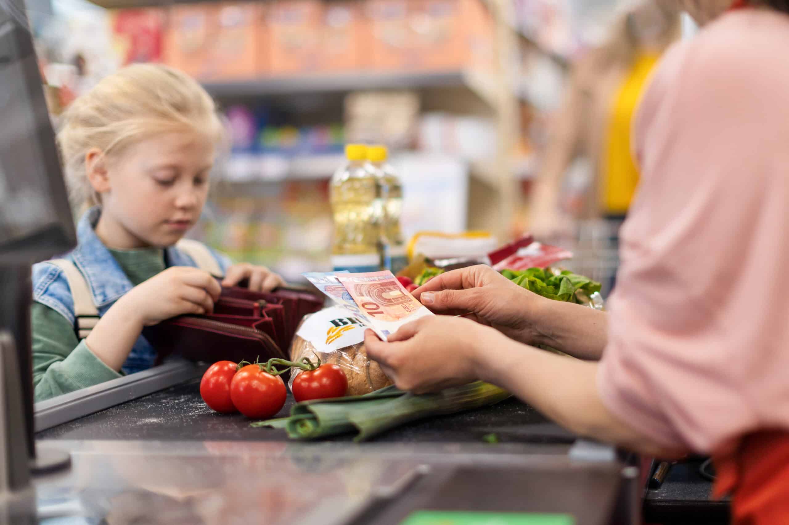 Gros plan sur une petite fille blonde qui paye ses courses au supermarché.